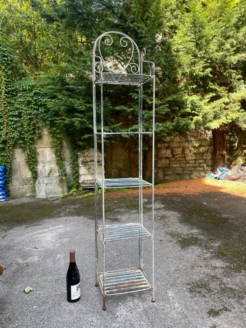 A tall, narrow painted metal plant stand with five slatted shelves and scrollwork decorative detailing at the top. View III