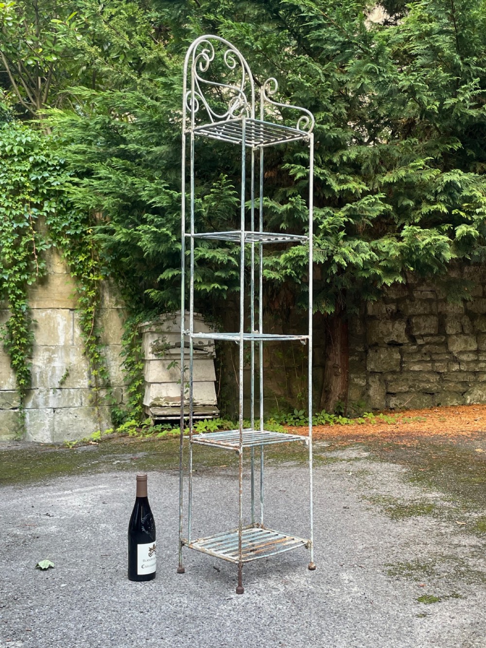 A tall, narrow painted metal plant stand with five slatted shelves and scrollwork decorative detailing at the top. View IV
