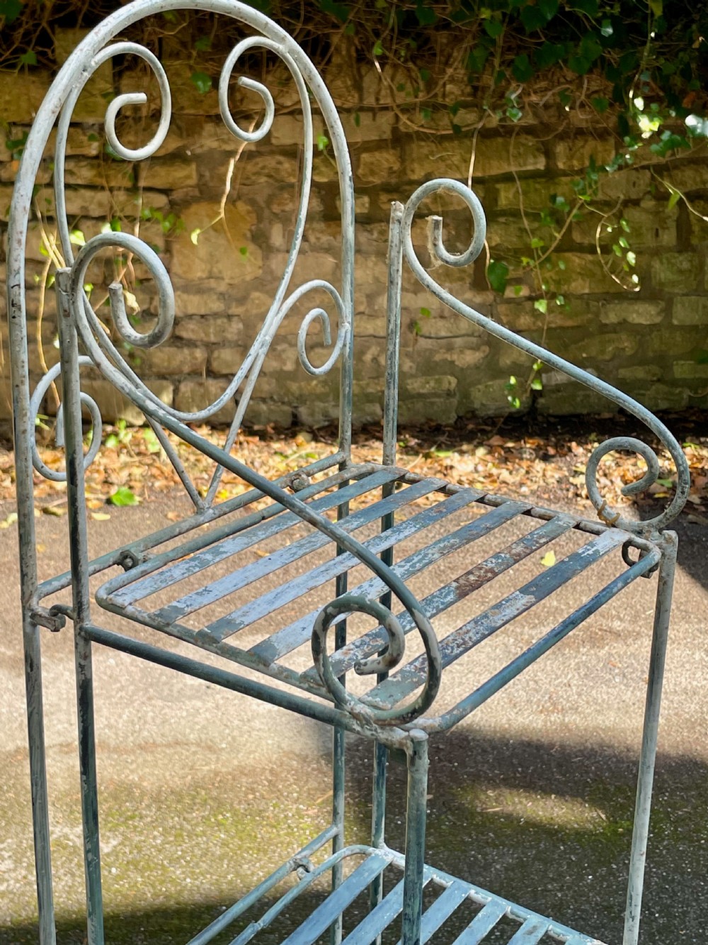 A tall, narrow painted metal plant stand with five slatted shelves and scrollwork decorative detailing at the top. View VIII