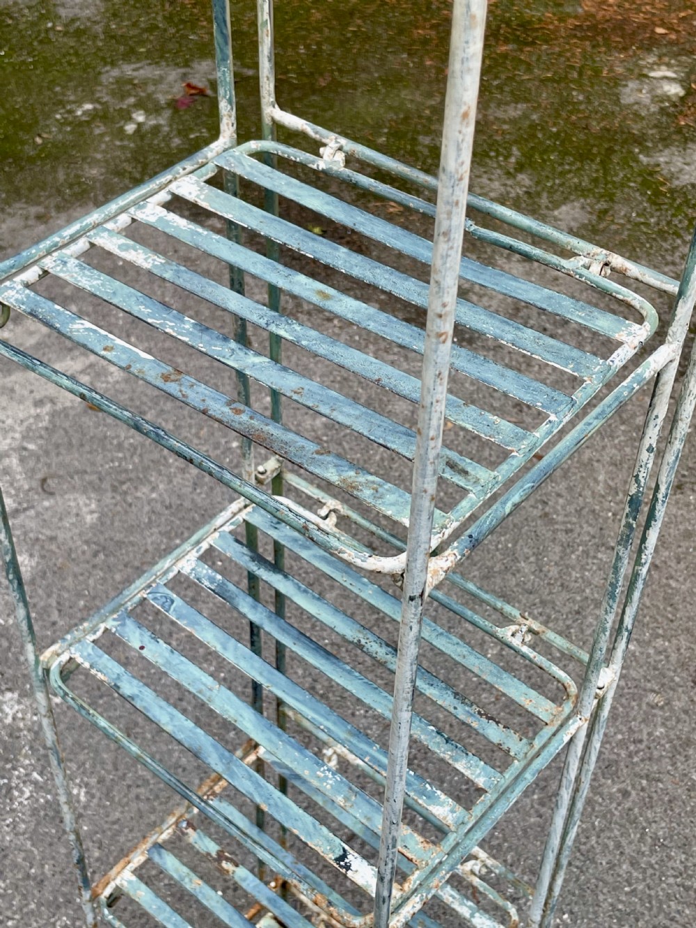 A tall, narrow painted metal plant stand with five slatted shelves and scrollwork decorative detailing at the top. View XI