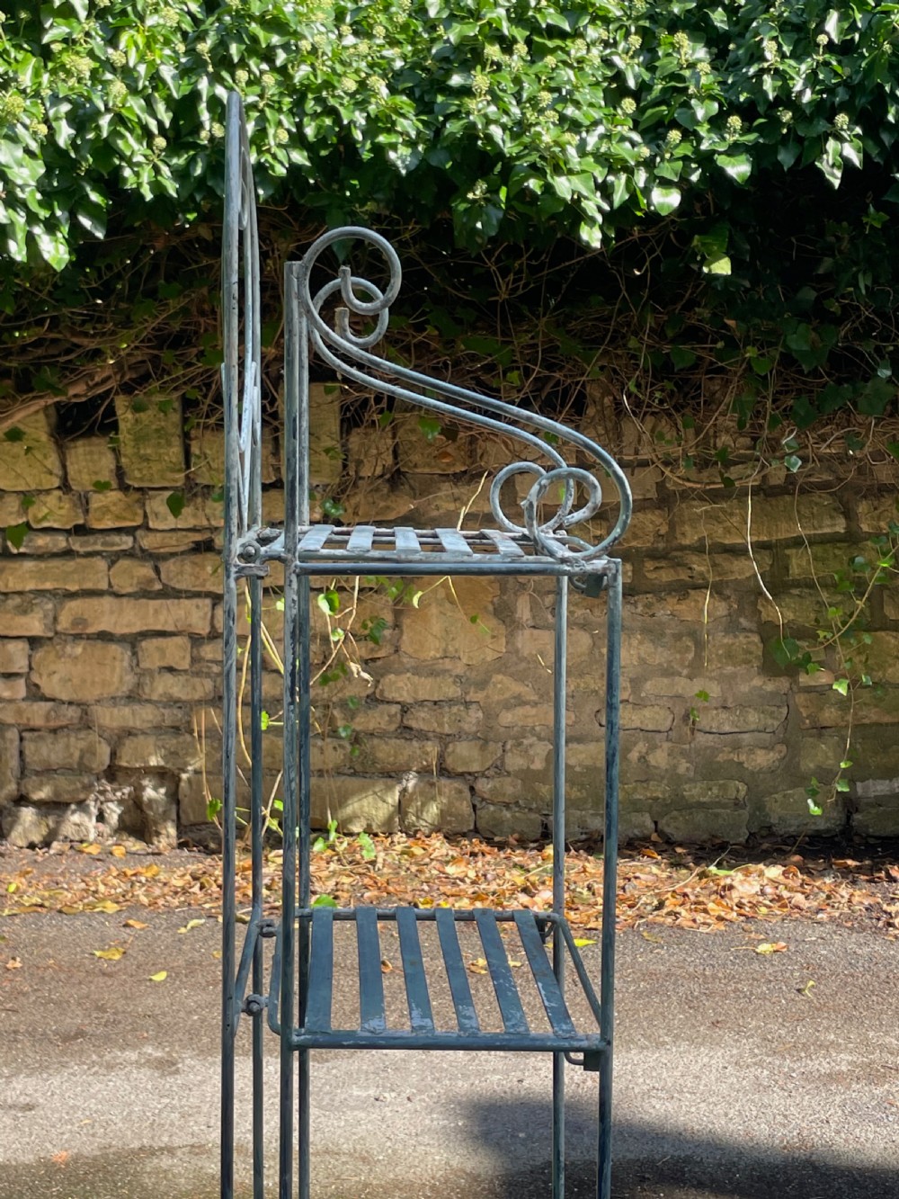 A tall, narrow painted metal plant stand with five slatted shelves and scrollwork decorative detailing at the top. View XII