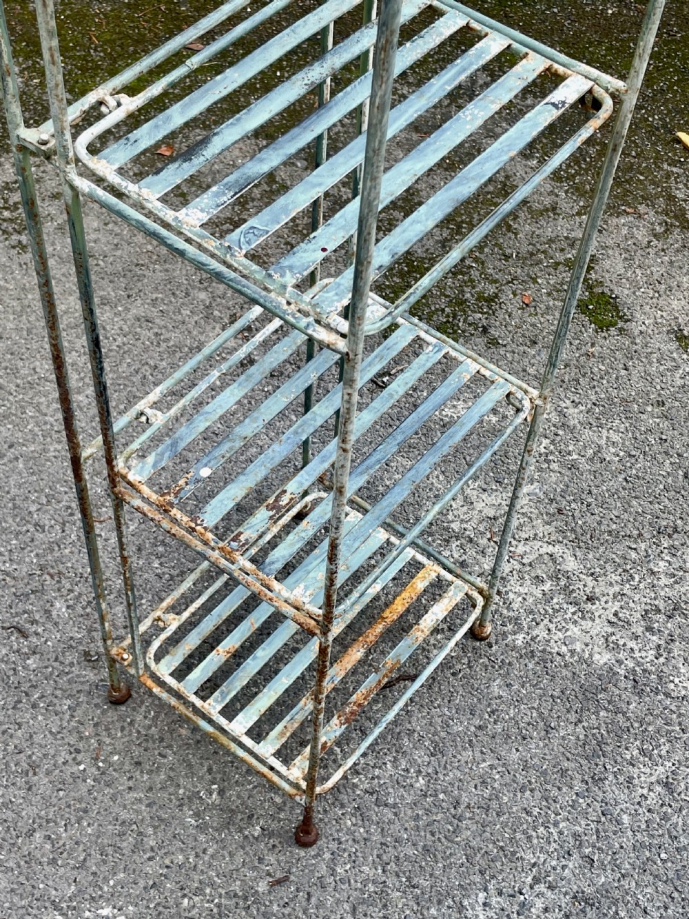 A tall, narrow painted metal plant stand with five slatted shelves and scrollwork decorative detailing at the top. View XIII