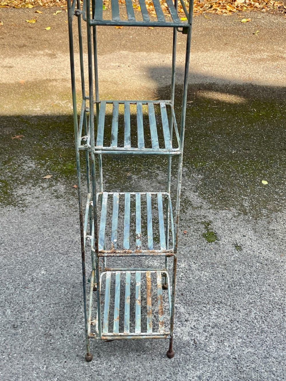 A tall, narrow painted metal plant stand with five slatted shelves and scrollwork decorative detailing at the top. View XV
