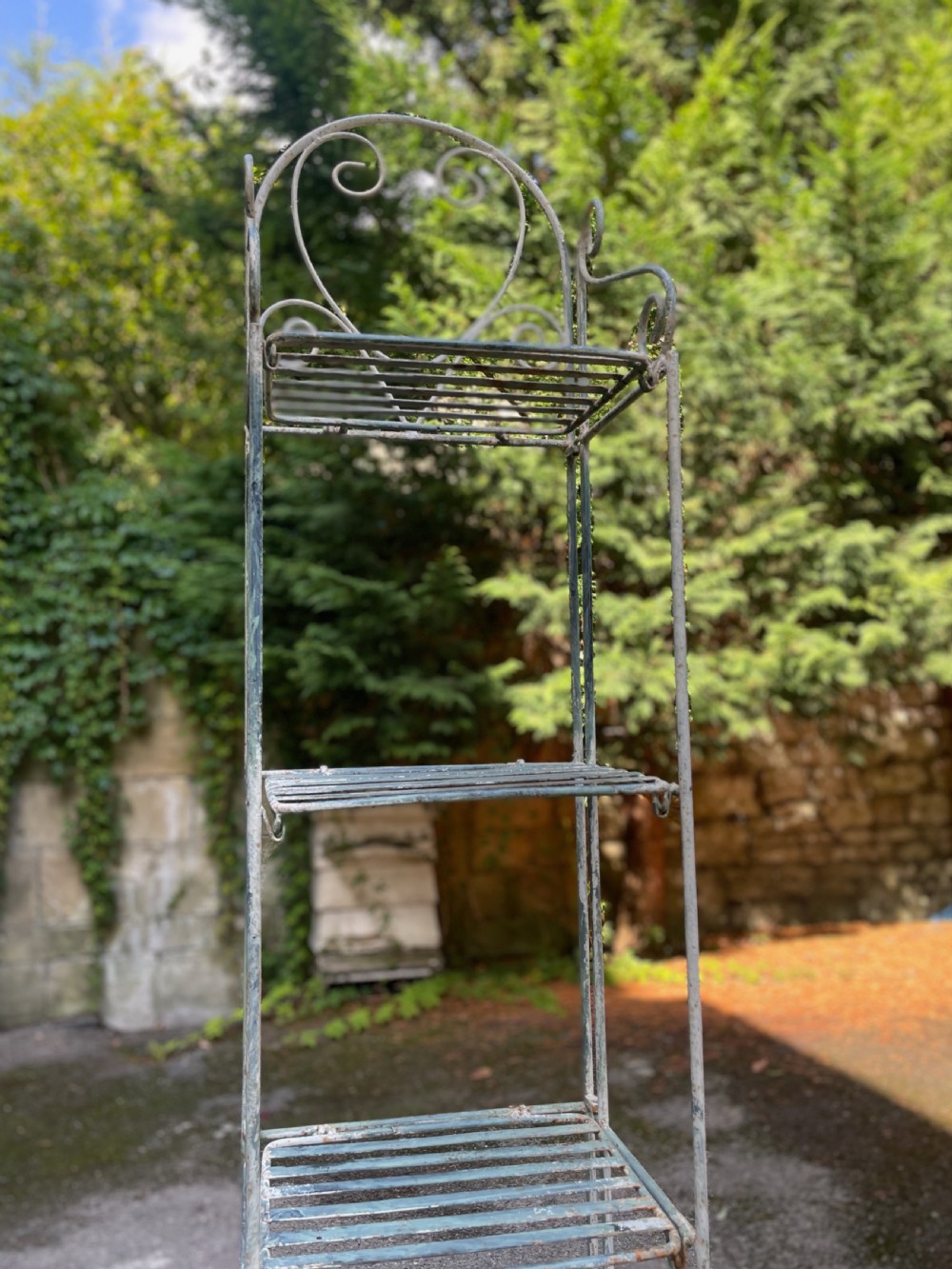 A tall, narrow painted metal plant stand with five slatted shelves and scrollwork decorative detailing at the top. View XVII