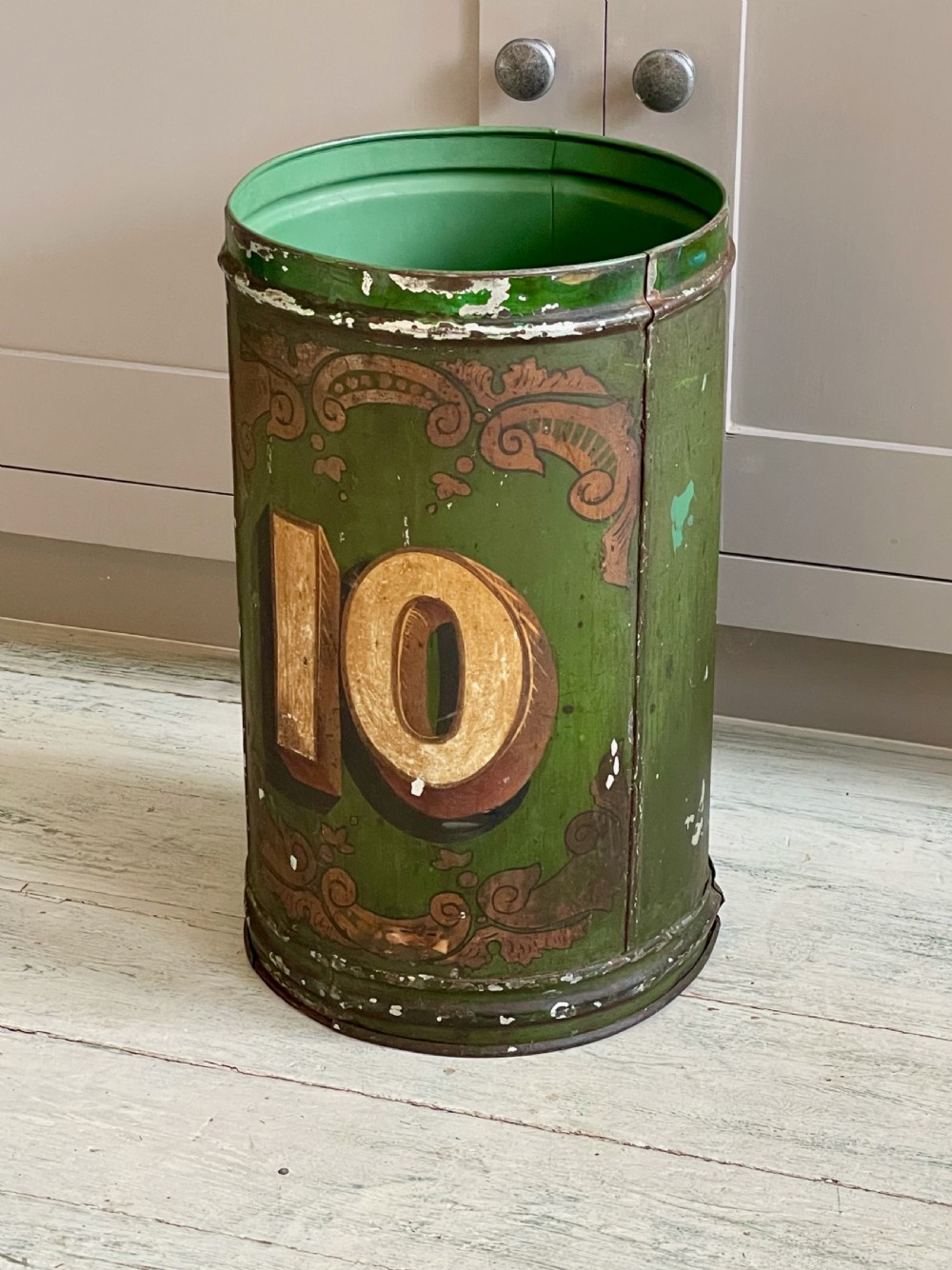 A cylindrical green painted antique metal tea canister featuring gold scrollwork and the painted number ten. View II
