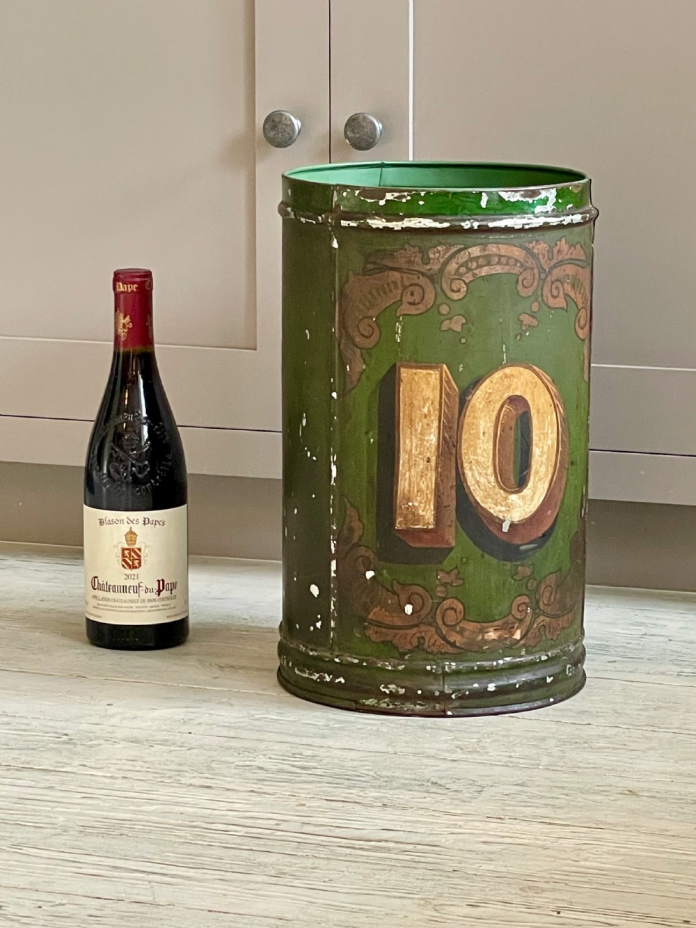 A cylindrical green painted antique metal tea canister featuring gold scrollwork and the painted number ten. View X