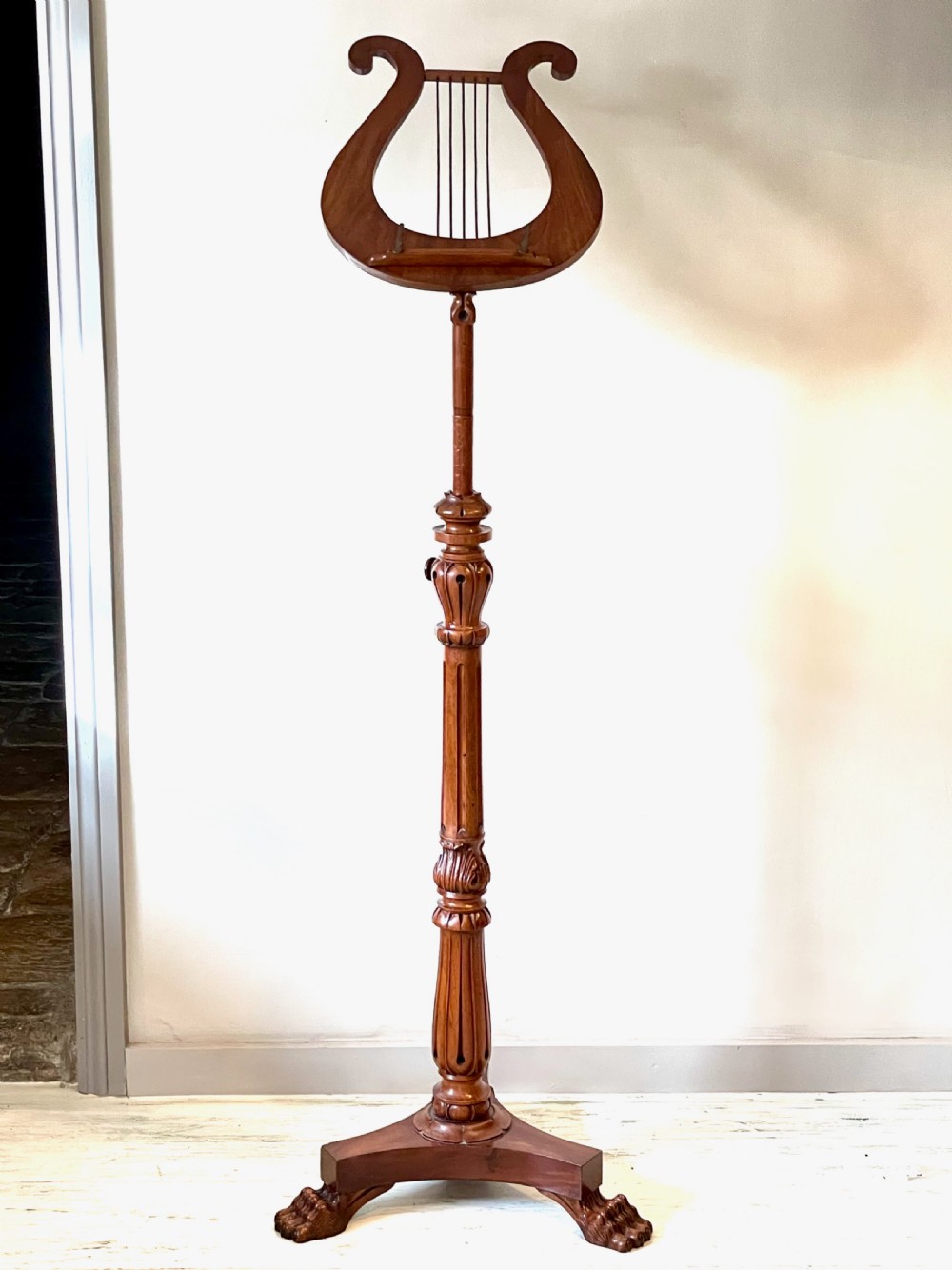 A nineteenth-century mahogany music stand featuring a lyre-shaped rest, a carved turned stem, and a triform base terminating in paw feet.