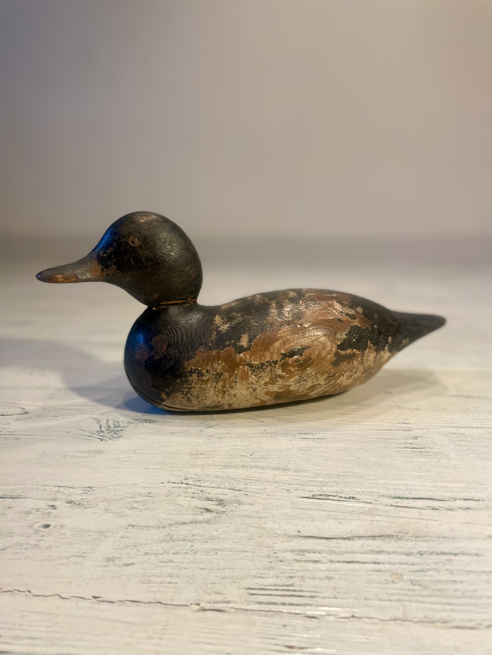 A hand-carved wooden duck decoy featuring weathered black and brown paint with exposed natural timber grain and a contoured head.