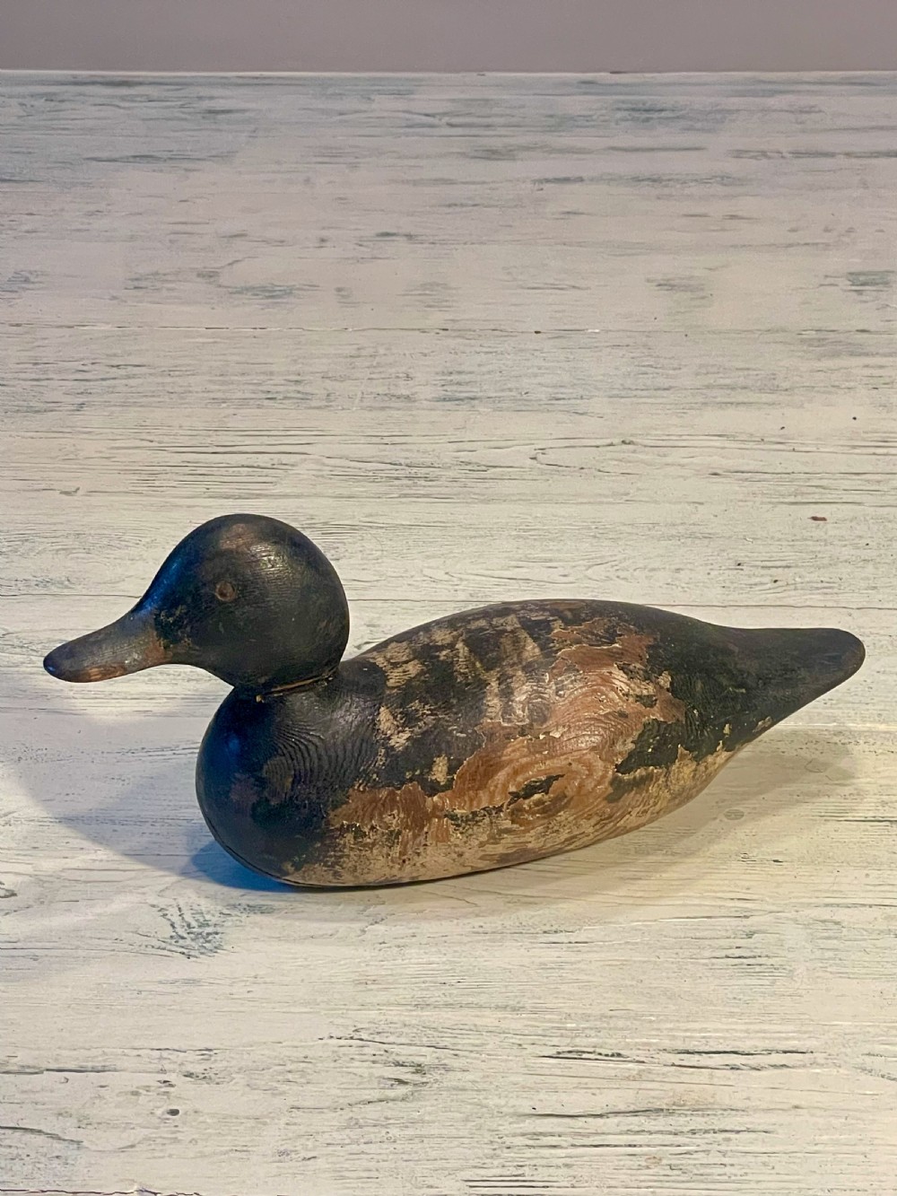 A hand-carved wooden duck decoy featuring weathered black and brown paint with exposed natural timber grain and a contoured head. View II