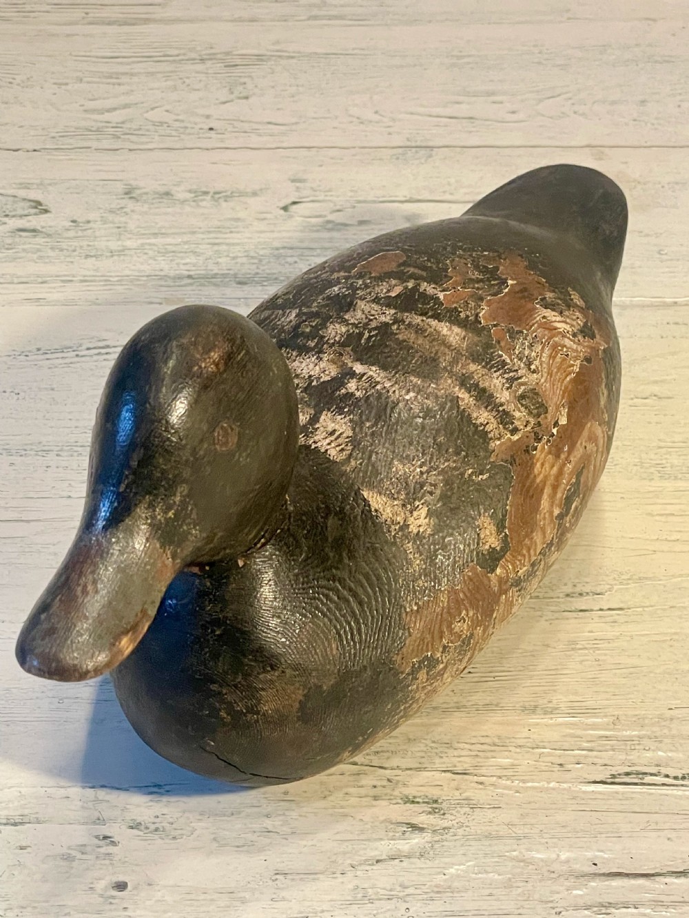 A hand-carved wooden duck decoy featuring weathered black and brown paint with exposed natural timber grain and a contoured head. View III