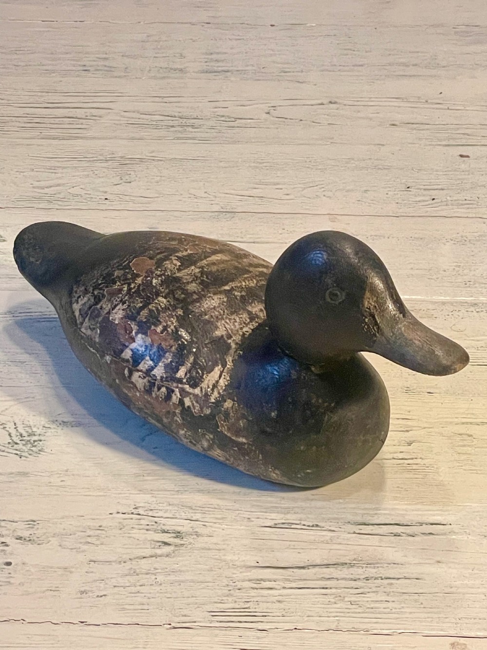 A hand-carved wooden duck decoy featuring weathered black and brown paint with exposed natural timber grain and a contoured head. View IV