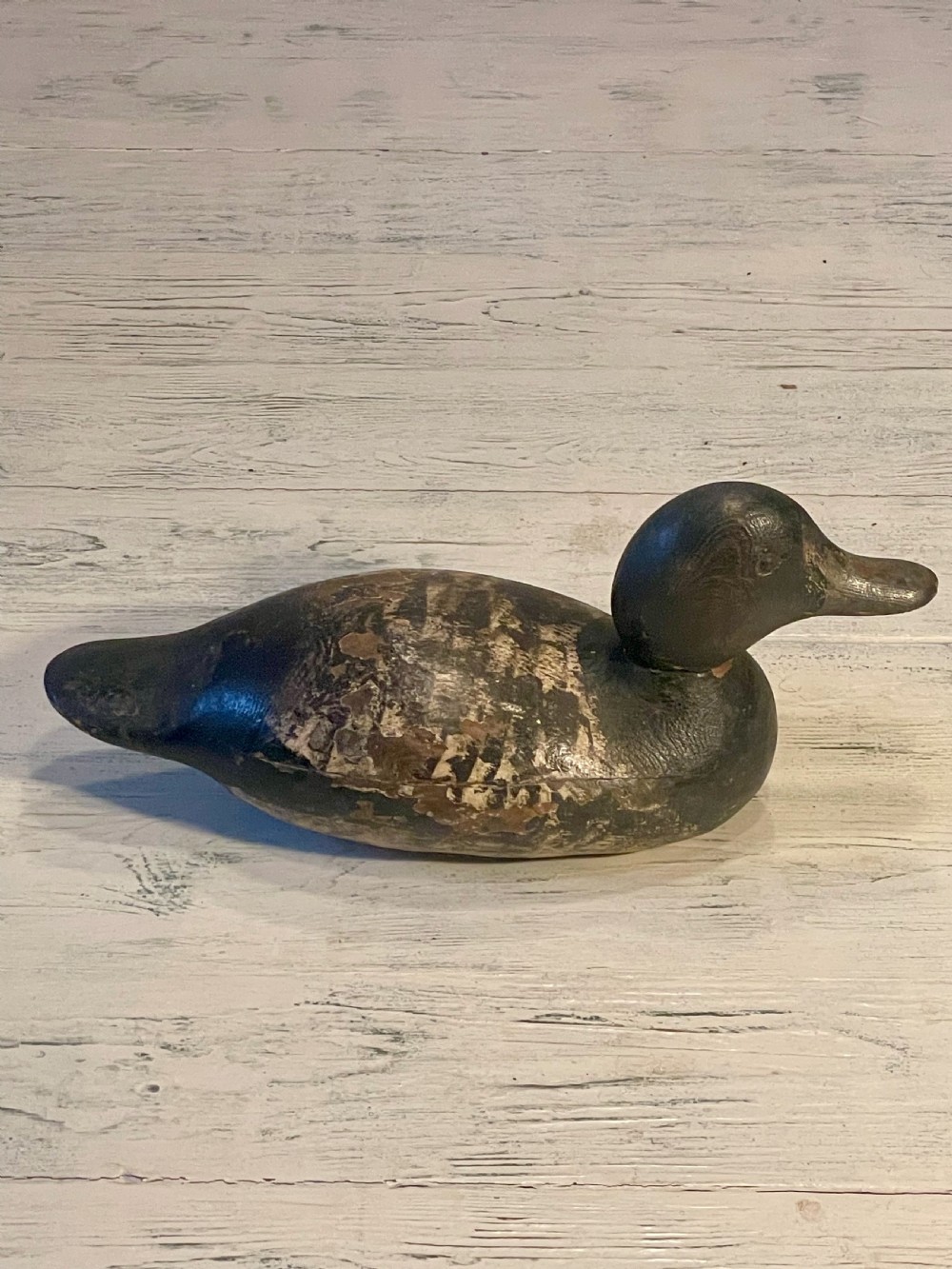 A hand-carved wooden duck decoy featuring weathered black and brown paint with exposed natural timber grain and a contoured head. View V
