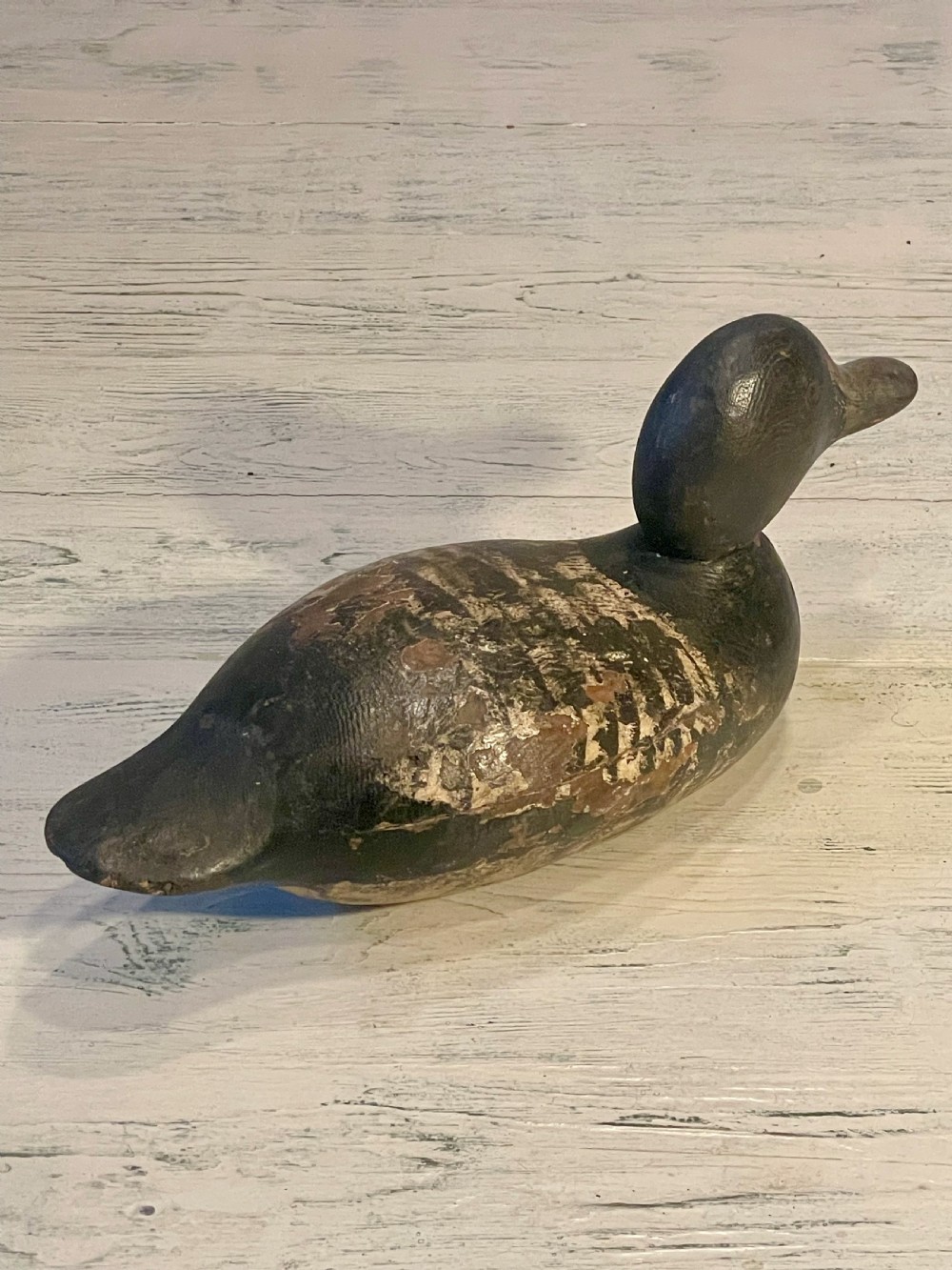 A hand-carved wooden duck decoy featuring weathered black and brown paint with exposed natural timber grain and a contoured head. View VI