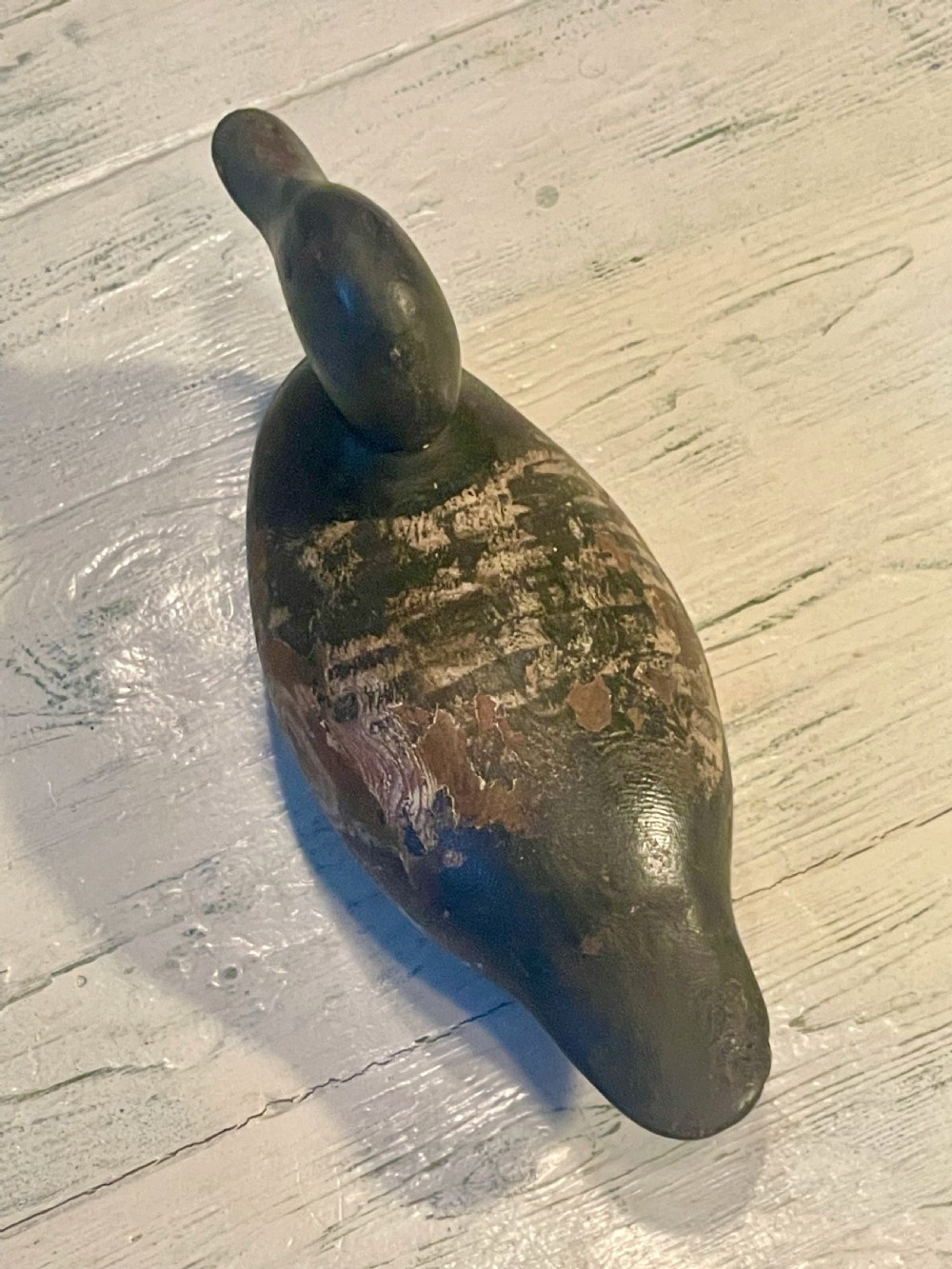 A hand-carved wooden duck decoy featuring weathered black and brown paint with exposed natural timber grain and a contoured head. View VII