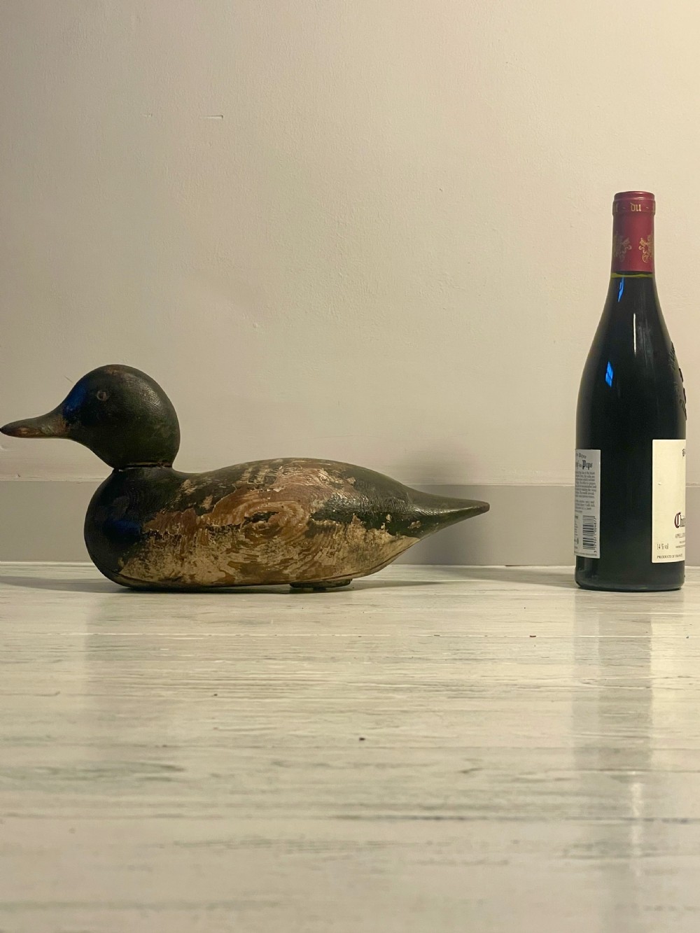 A hand-carved wooden duck decoy featuring weathered black and brown paint with exposed natural timber grain and a contoured head. View X
