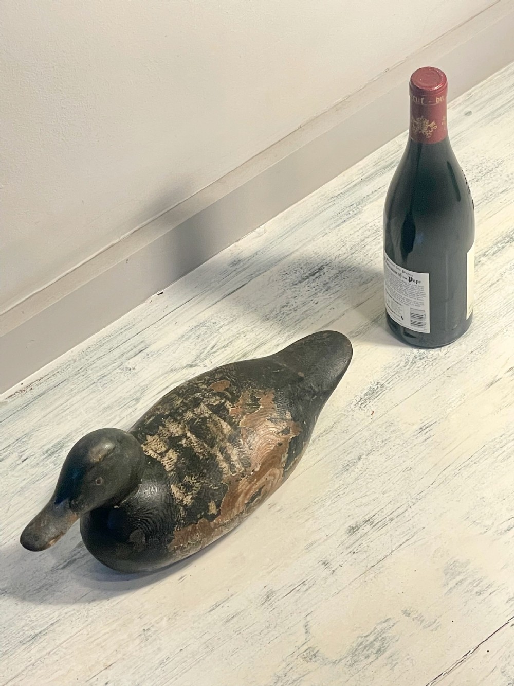 A hand-carved wooden duck decoy featuring weathered black and brown paint with exposed natural timber grain and a contoured head. View XI