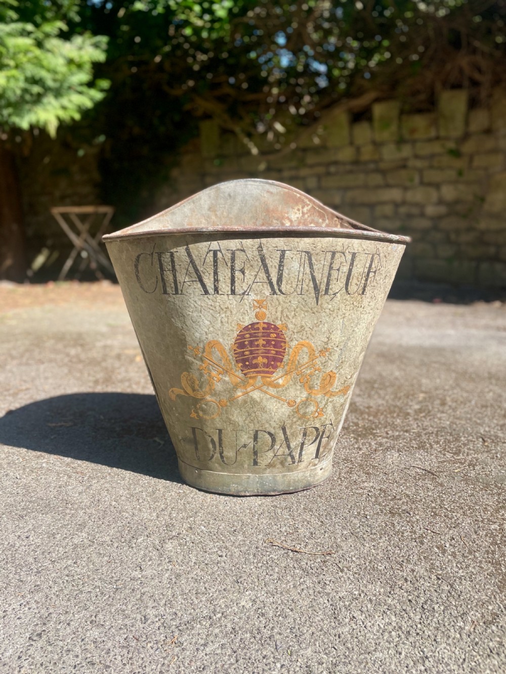 A tapered 19th-century metal grape hod featuring a distressed beige finish with hand-painted Chateauneuf-du-Pape lettering and a papal crest.
