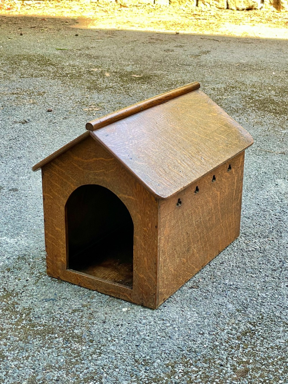 An antique Victorian warm brown oak dog kennel featuring a pitched roof, arched entrance aperture, and trefoil ventilation cutouts along the side. View II