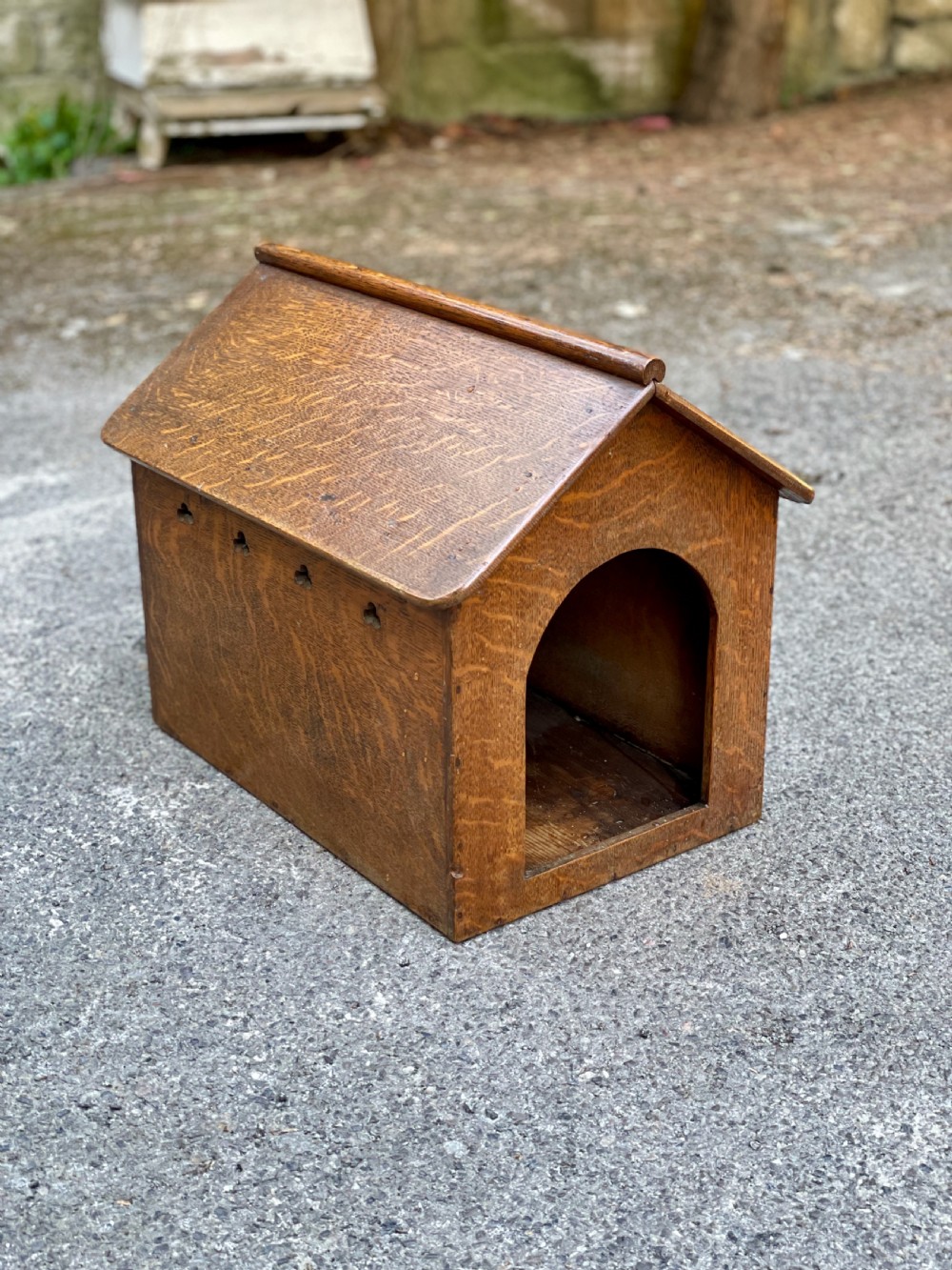 An antique Victorian warm brown oak dog kennel featuring a pitched roof, arched entrance aperture, and trefoil ventilation cutouts along the side. View III