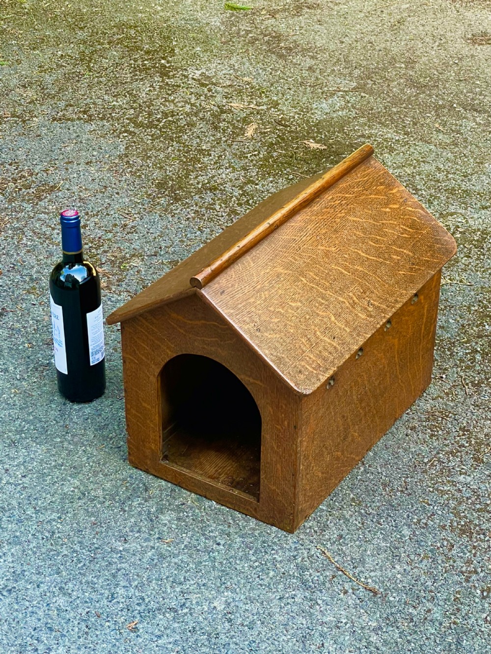 An antique Victorian warm brown oak dog kennel featuring a pitched roof, arched entrance aperture, and trefoil ventilation cutouts along the side. View X