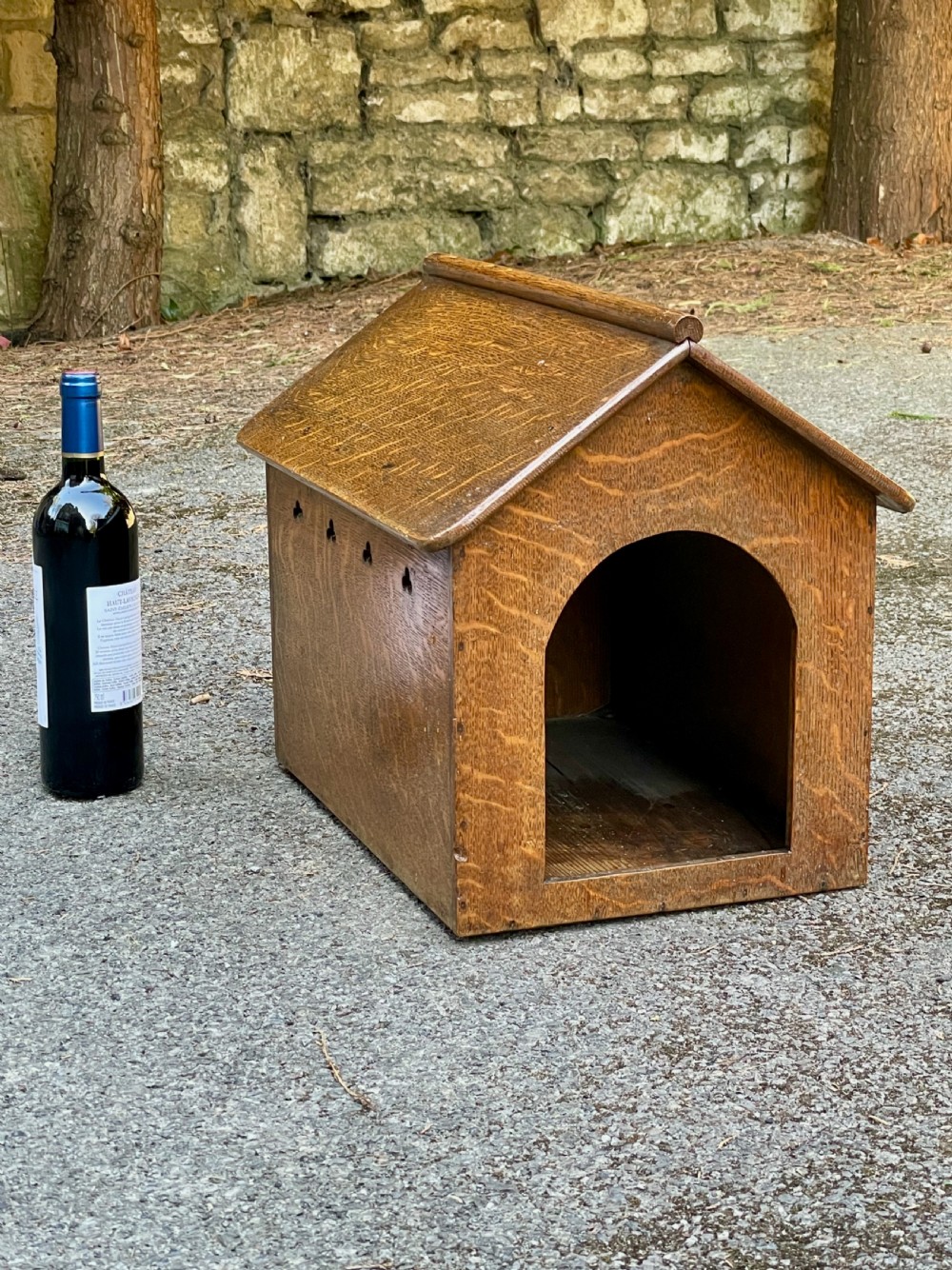 An antique Victorian warm brown oak dog kennel featuring a pitched roof, arched entrance aperture, and trefoil ventilation cutouts along the side. View XI