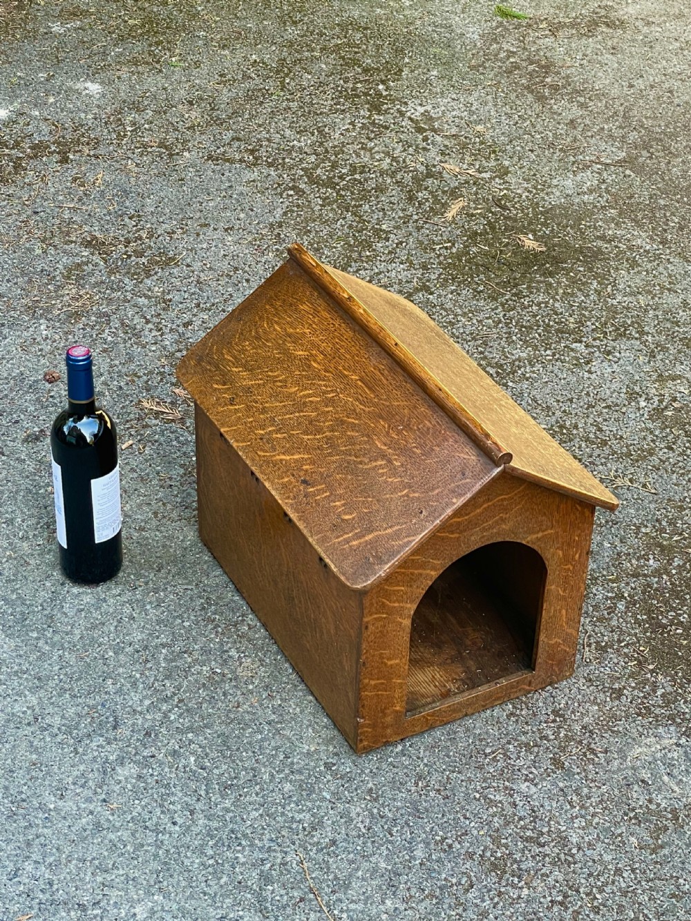 An antique Victorian warm brown oak dog kennel featuring a pitched roof, arched entrance aperture, and trefoil ventilation cutouts along the side. View XII