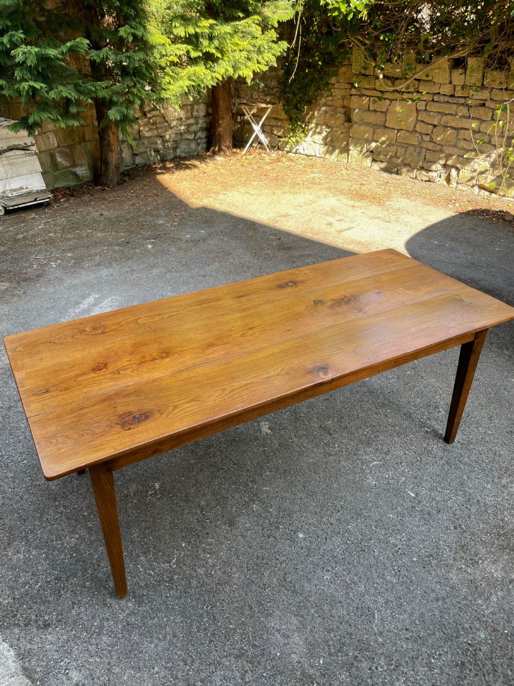 A long wooden refectory dining table constructed with a three-plank top and four square tapered legs.