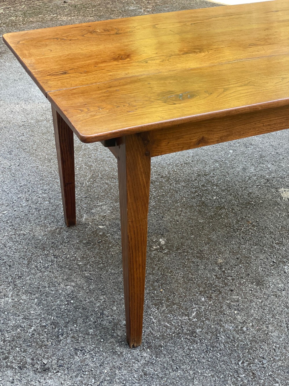 A long wooden refectory dining table constructed with a three-plank top and four square tapered legs. View II