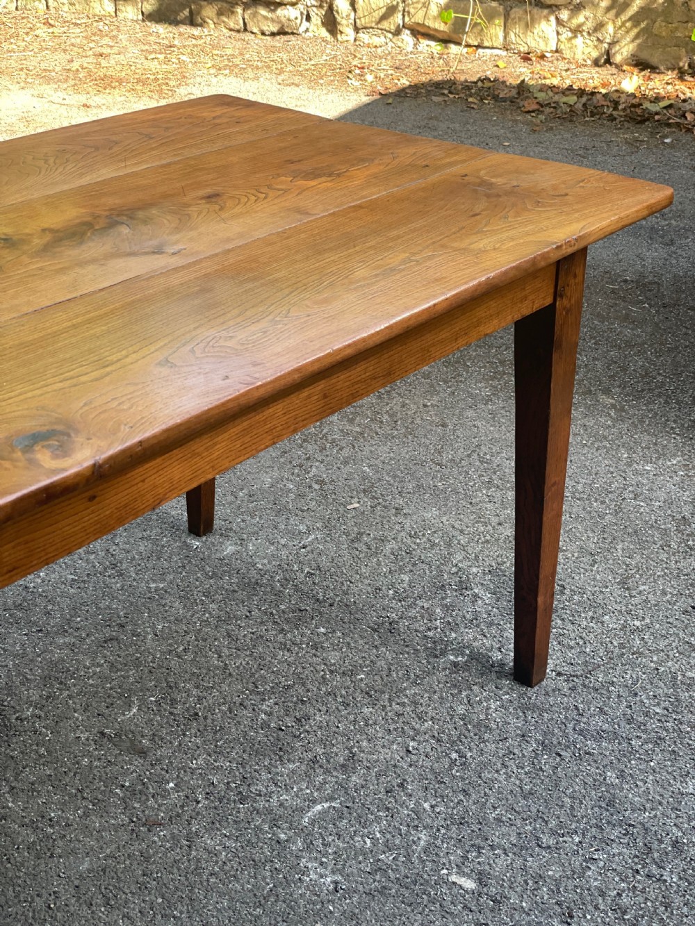 A long wooden refectory dining table constructed with a three-plank top and four square tapered legs. View III