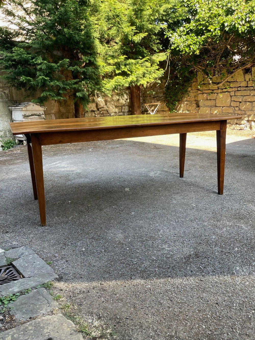 A long wooden refectory dining table constructed with a three-plank top and four square tapered legs. View IV