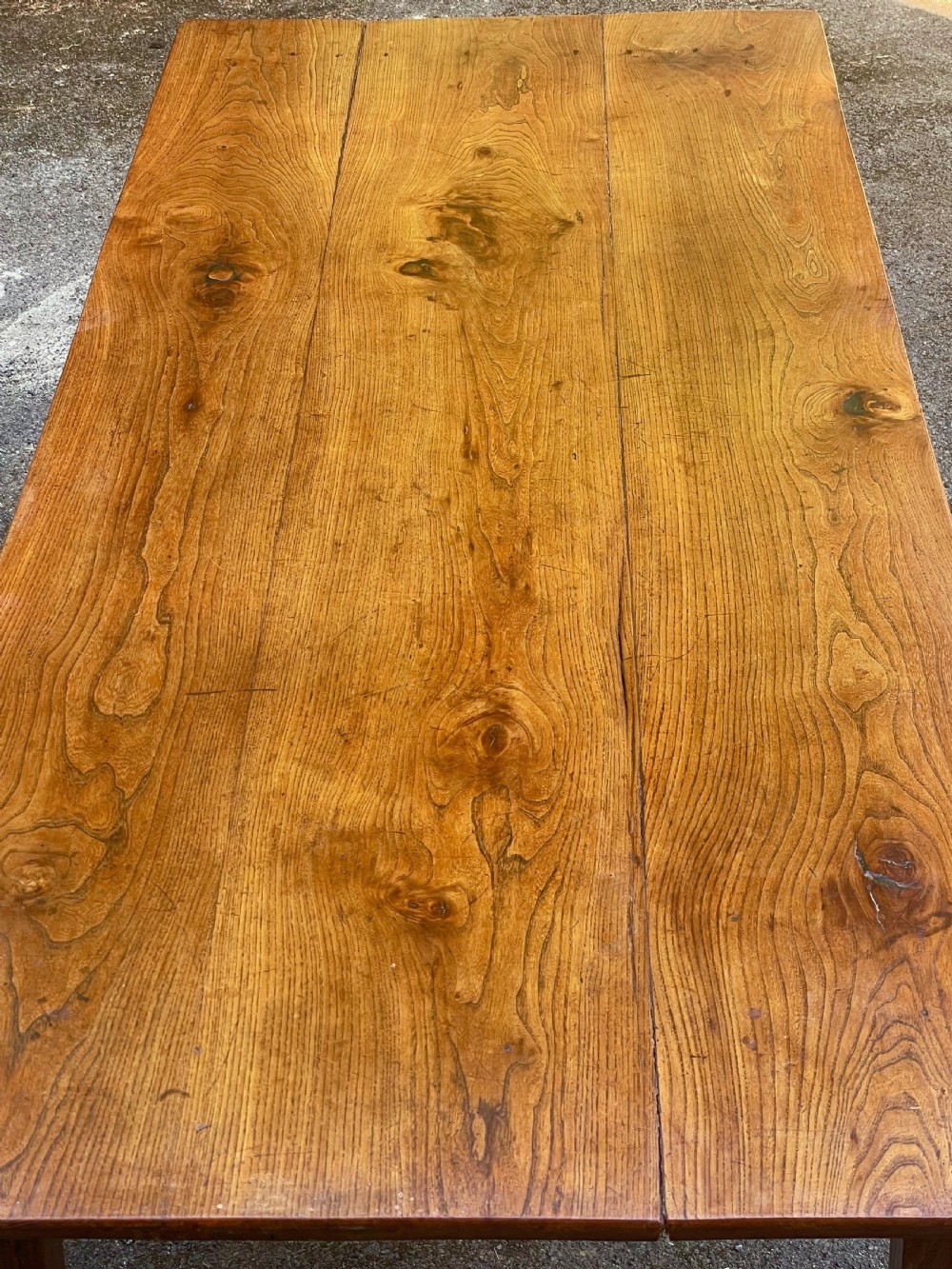 A long wooden refectory dining table constructed with a three-plank top and four square tapered legs. View VII