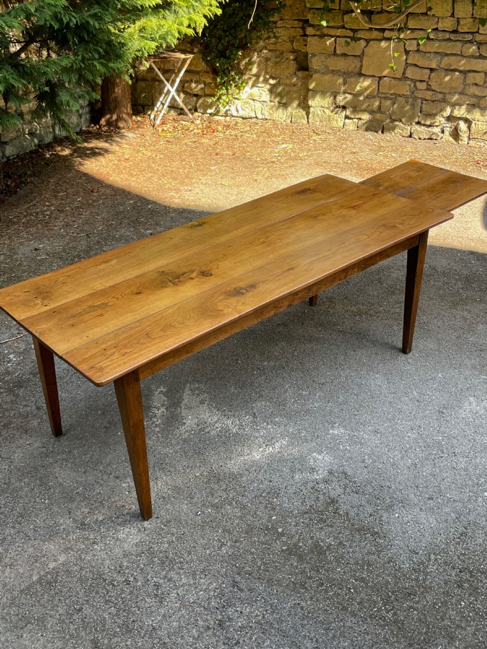 A long wooden refectory dining table constructed with a three-plank top and four square tapered legs. View IX