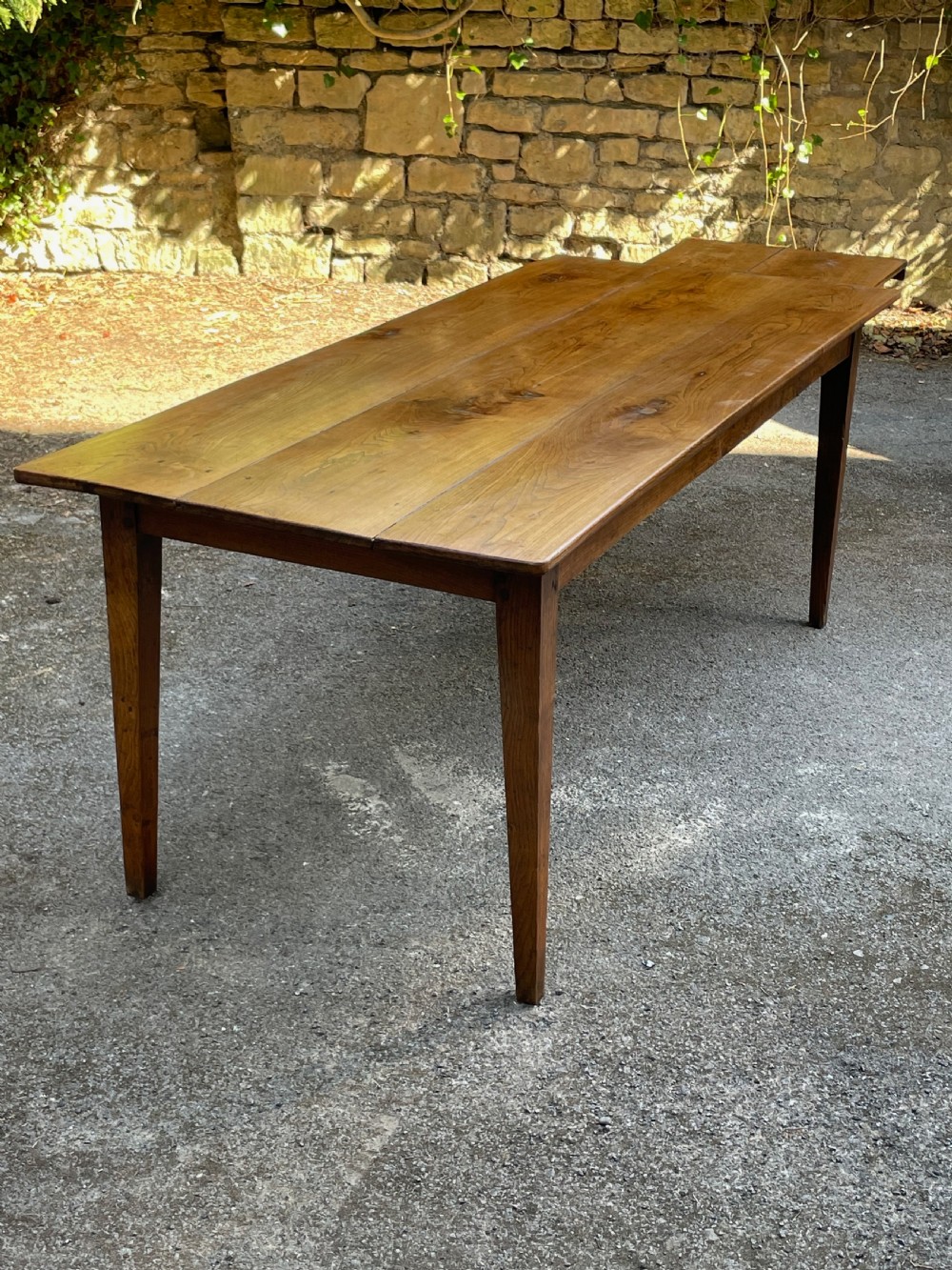 A long wooden refectory dining table constructed with a three-plank top and four square tapered legs. View XI