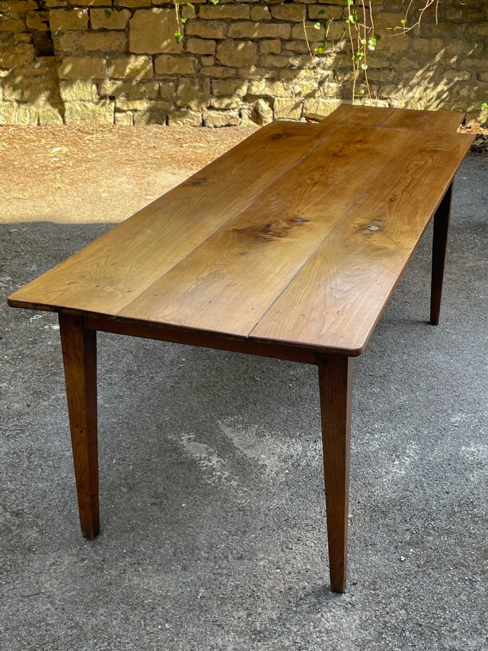 A long wooden refectory dining table constructed with a three-plank top and four square tapered legs. View XII