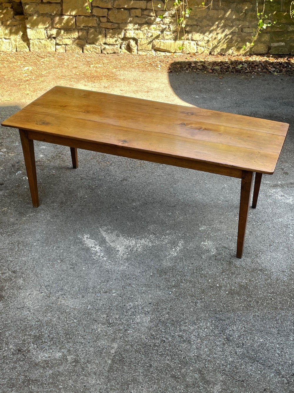 A long wooden refectory dining table constructed with a three-plank top and four square tapered legs. View XV