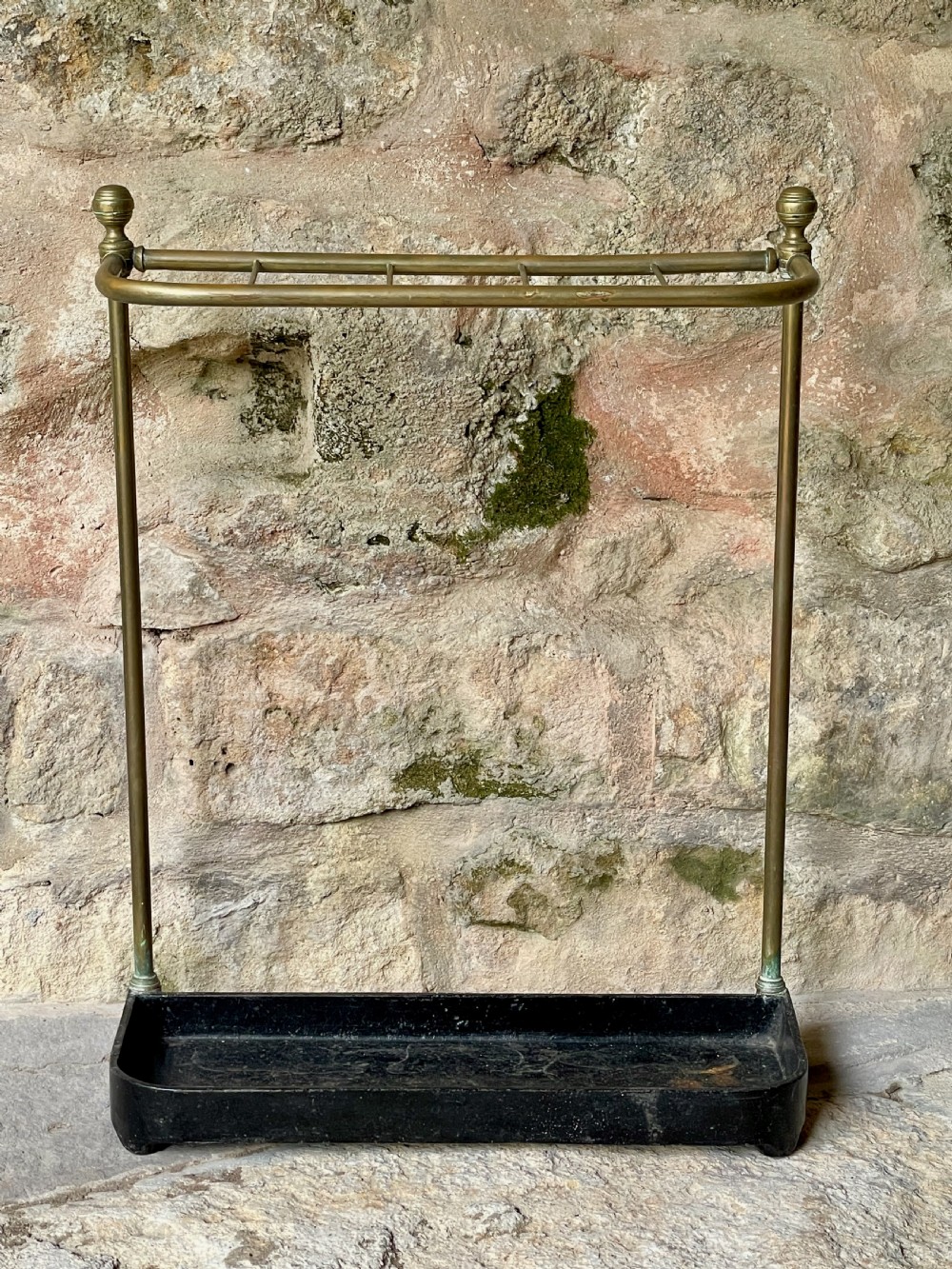 An antique Edwardian brass stick stand featuring a divided top rail with urn finials and a black cast iron drip tray base. View III