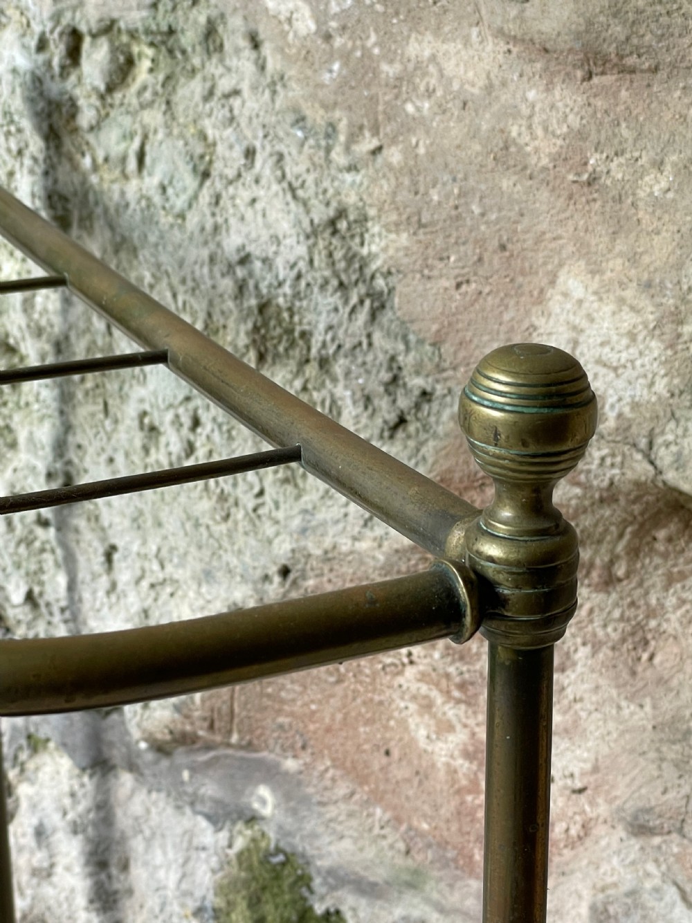An antique Edwardian brass stick stand featuring a divided top rail with urn finials and a black cast iron drip tray base. View VII