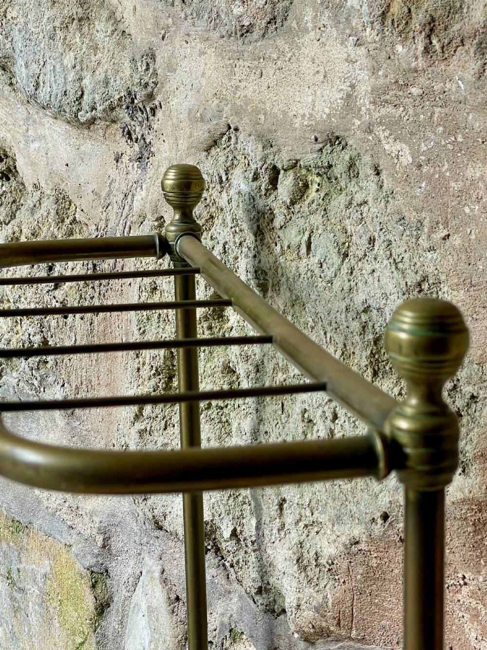 An antique Edwardian brass stick stand featuring a divided top rail with urn finials and a black cast iron drip tray base. View VIII