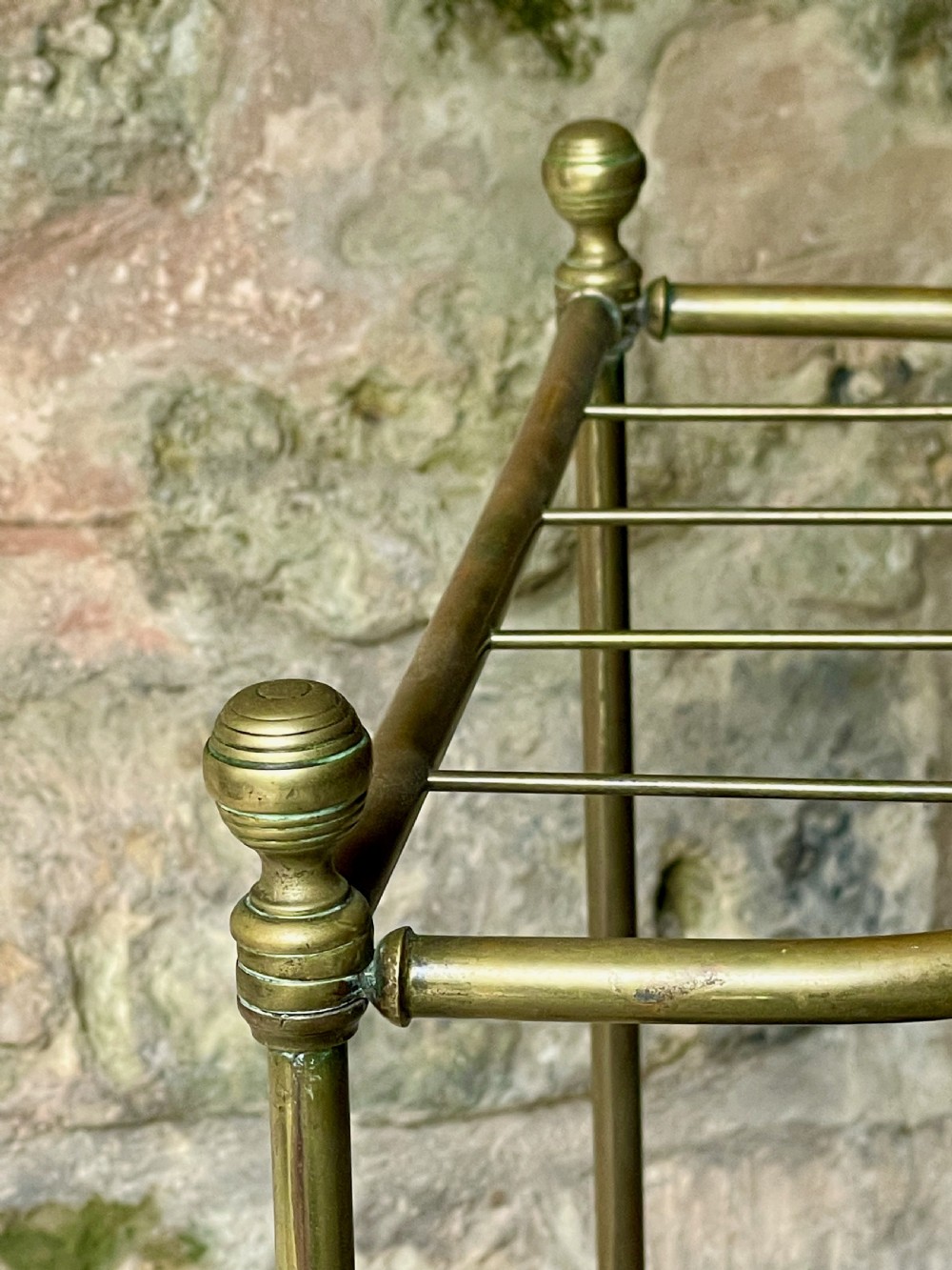 An antique Edwardian brass stick stand featuring a divided top rail with urn finials and a black cast iron drip tray base. View XII
