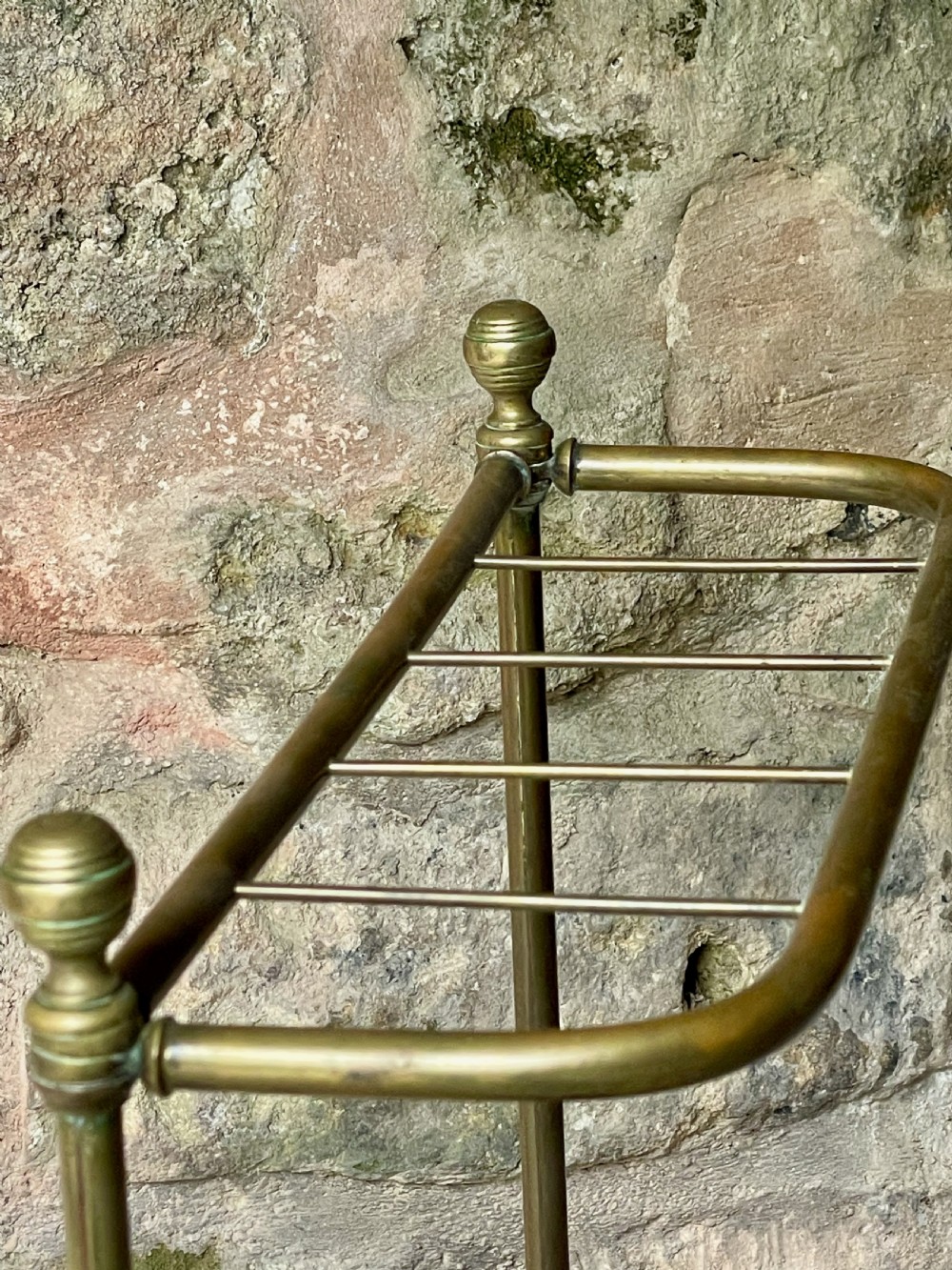 An antique Edwardian brass stick stand featuring a divided top rail with urn finials and a black cast iron drip tray base. View XIII