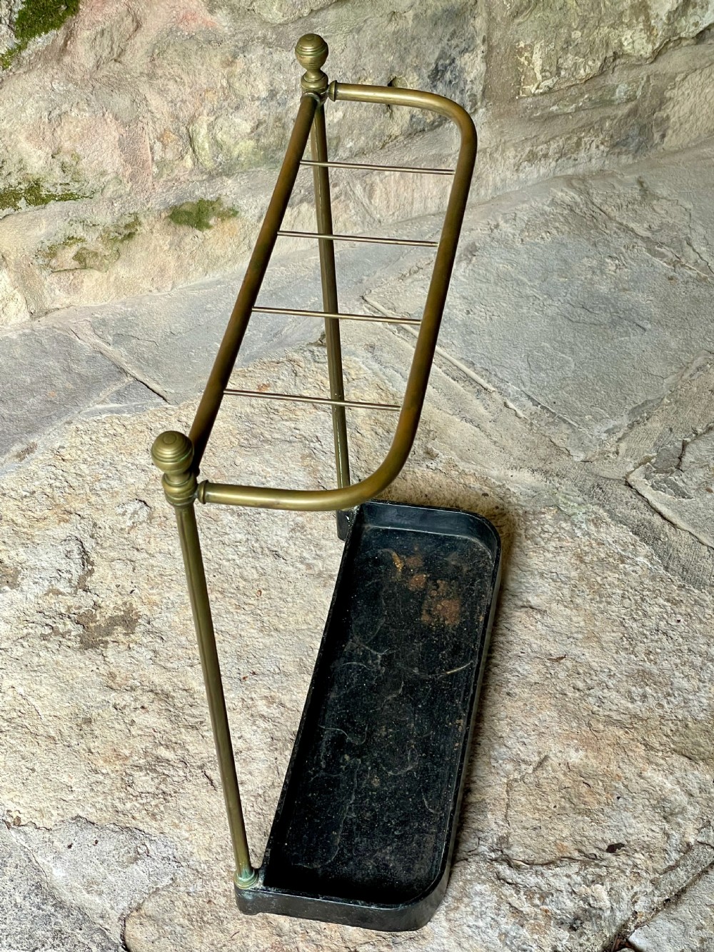 An antique Edwardian brass stick stand featuring a divided top rail with urn finials and a black cast iron drip tray base. View XIV