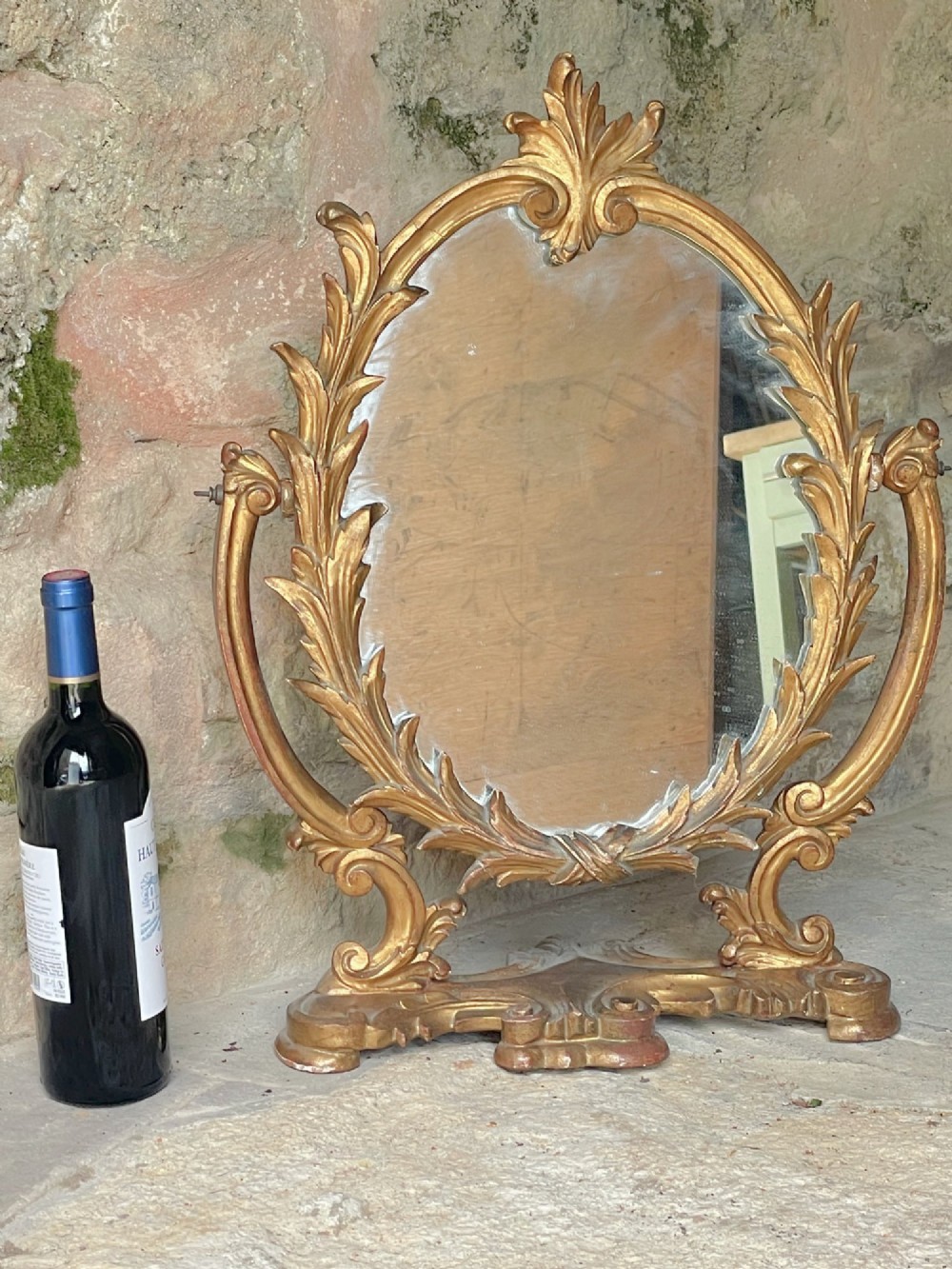 A carved giltwood toilet mirror with an oval pivoting mirror frame set on a decorative scrolling base. View II