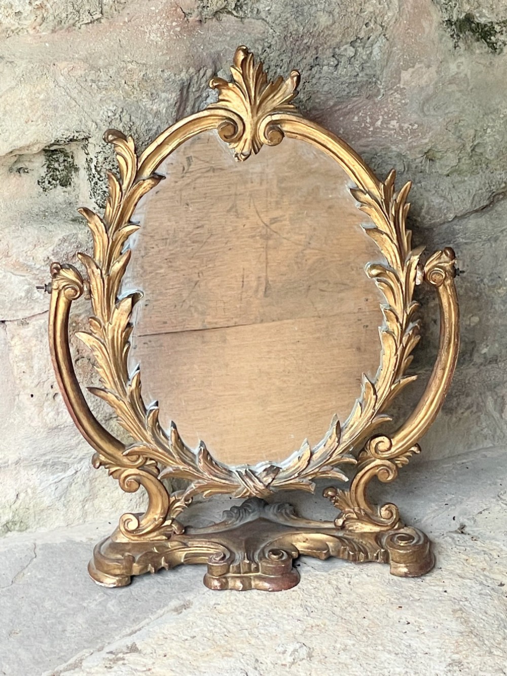 A carved giltwood toilet mirror with an oval pivoting mirror frame set on a decorative scrolling base. View III