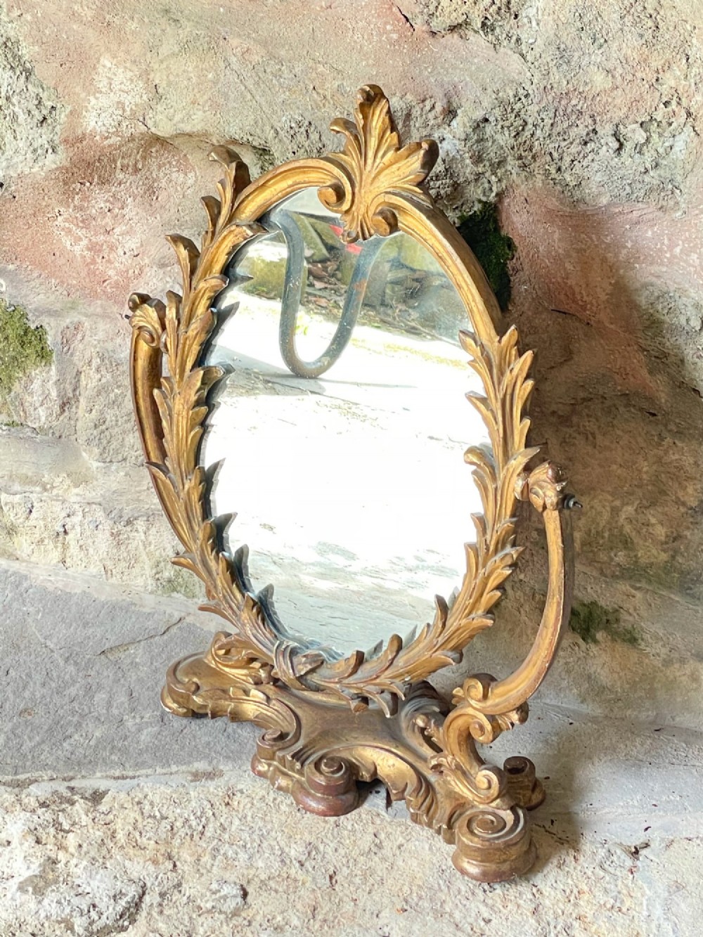 A carved giltwood toilet mirror with an oval pivoting mirror frame set on a decorative scrolling base. View V
