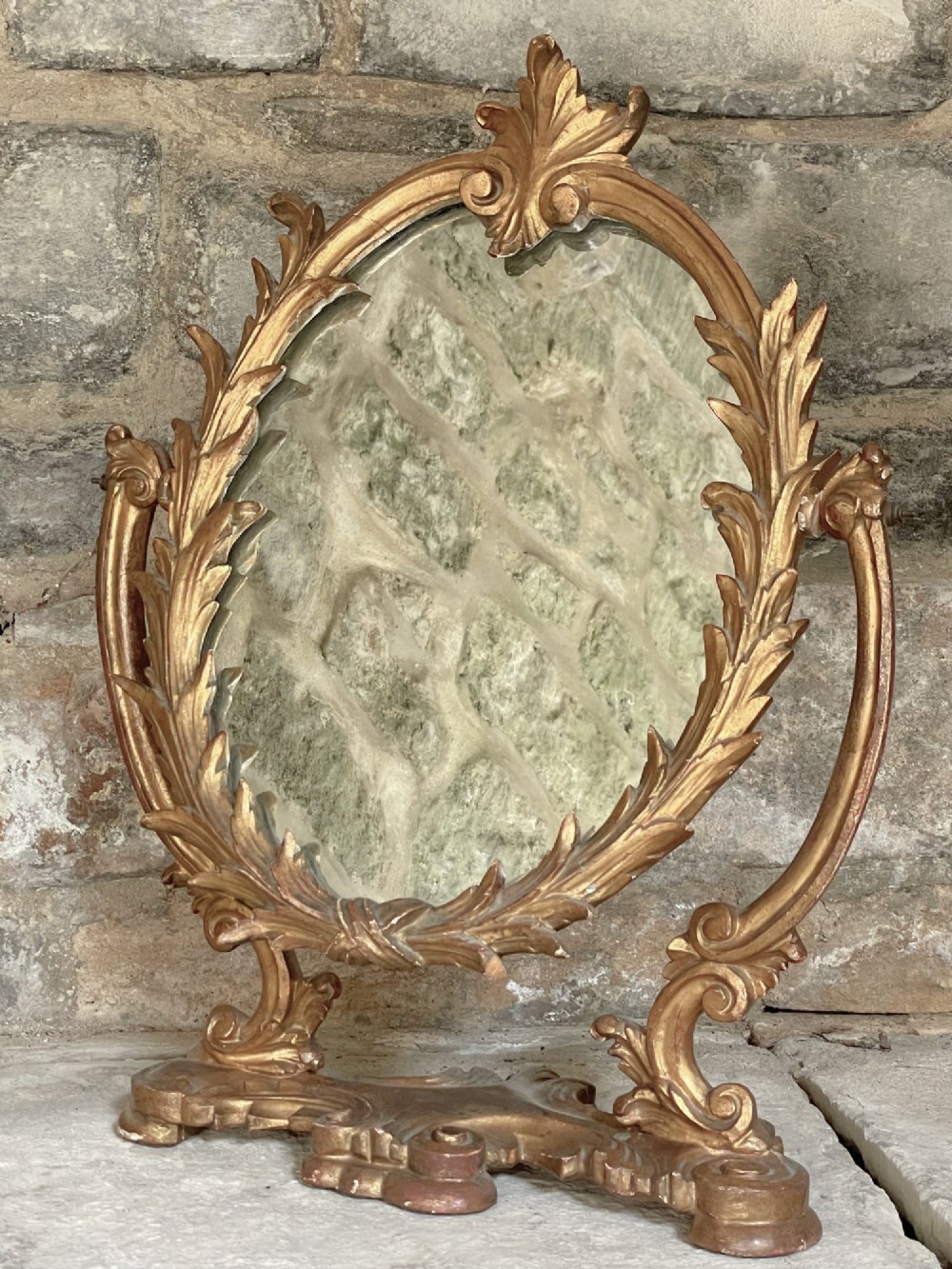 A carved giltwood toilet mirror with an oval pivoting mirror frame set on a decorative scrolling base. View VI