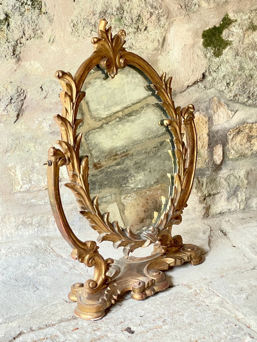 A carved giltwood toilet mirror with an oval pivoting mirror frame set on a decorative scrolling base. View VII