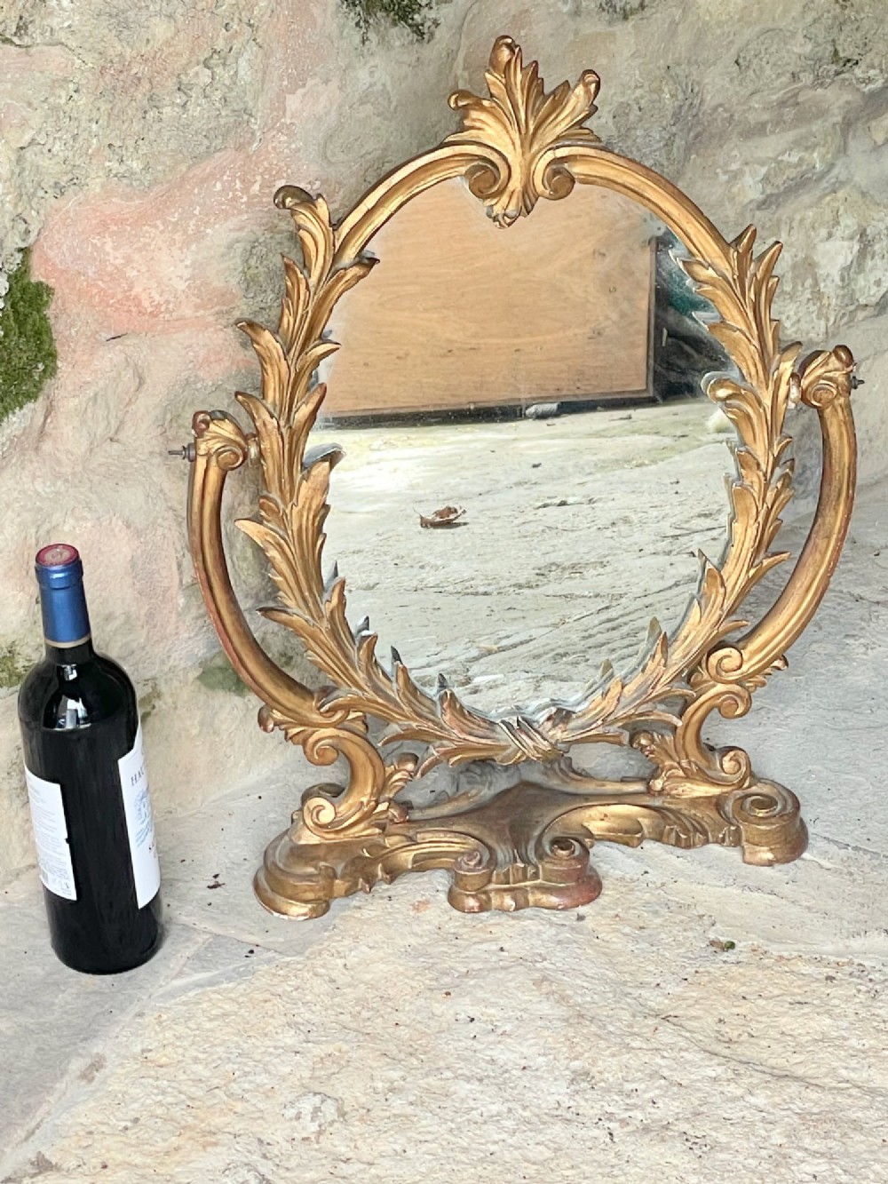 A carved giltwood toilet mirror with an oval pivoting mirror frame set on a decorative scrolling base. View IX
