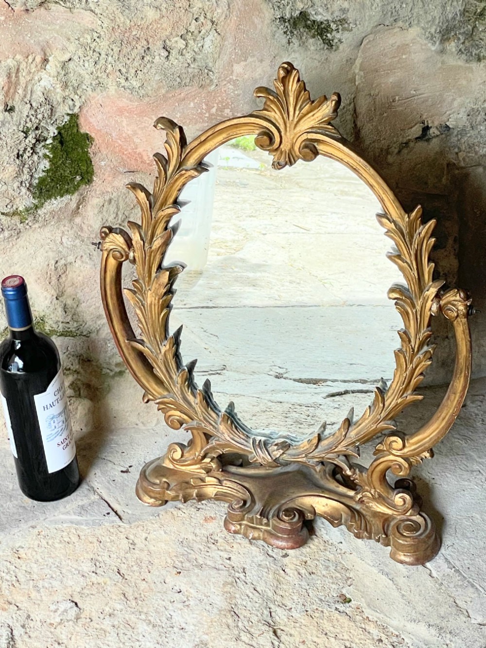 A carved giltwood toilet mirror with an oval pivoting mirror frame set on a decorative scrolling base. View X