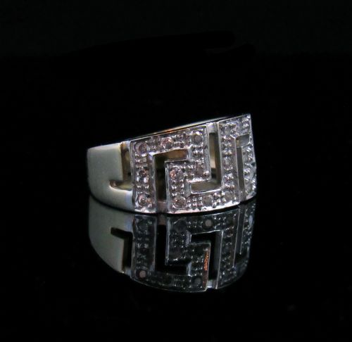 fig 1. A wide white gold band ring featuring a geometric Aztec pattern set with diamonds worn on a hand.