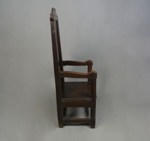 fig 1. A 17th-century Jacobean dark oak wainscot armchair featuring a high panelled back, straight arms, and heavy square legs joined by stretchers.